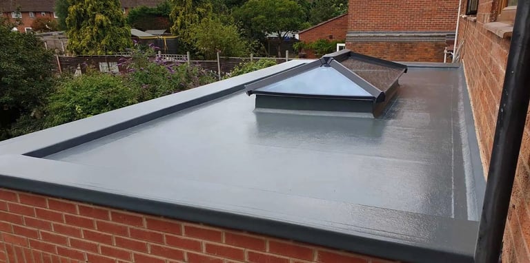 Modern flat roof with gray membrane and black trim installed on brick building, residential area visible beyond