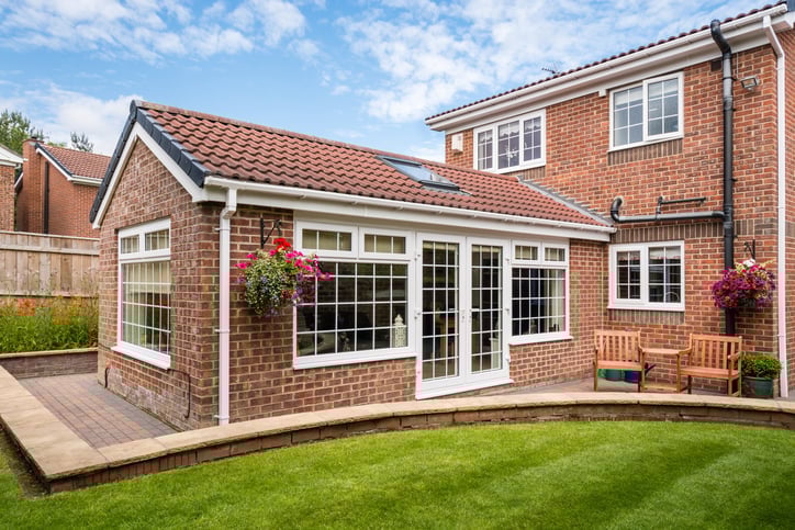 Modern brick home with white-framed conservatory, patio, and landscaped garden in sunny residential setting