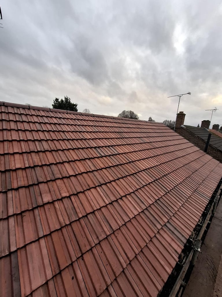 Aerial view of a terracotta tiled residential roof with chimneys and TV antennas against a cloudy sky