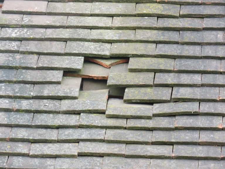 Damaged roof shingles with several missing tiles exposing the underlayment and wood structure beneath