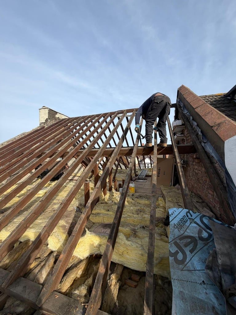 Roofer working on exposed wooden roof rafters of a brick building during renovation