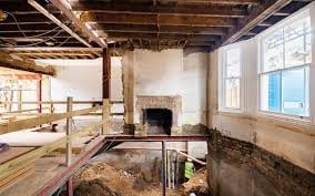 Industrial loft interior under renovation with exposed ceiling beams, brick fireplace, wooden framework, and large windows