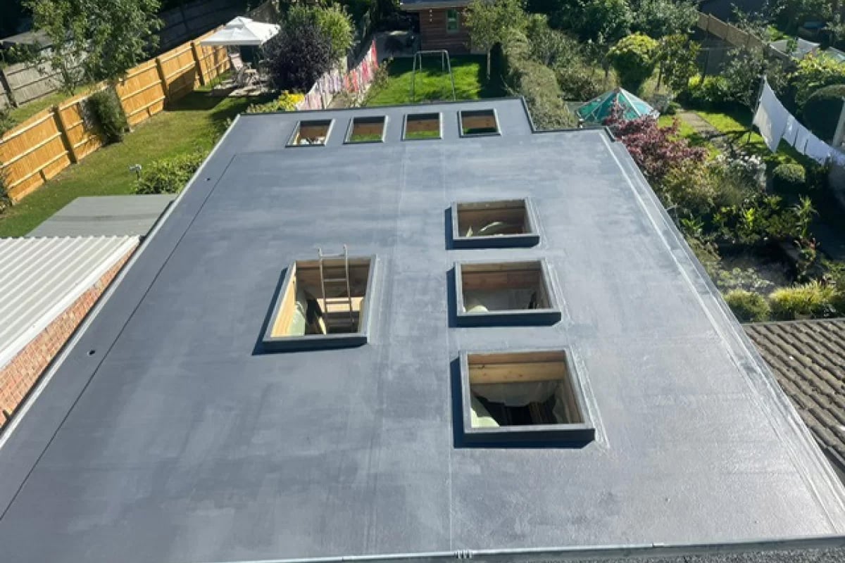 Aerial view of a flat roof with three square skylights, surrounded by residential yards and green spaces