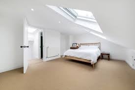 Bright attic bedroom with sloped ceiling, skylights, wooden bed, white walls, and beige flooring