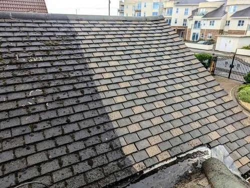 Close-up view of a residential roof with gray asphalt shingles and neighboring houses in the background