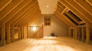 Bright attic space with wooden beam framing, exposed studs, and hardwood flooring under construction