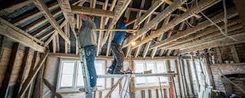 Interior view of house under construction showing wooden framing, exposed beams, and windows during renovation