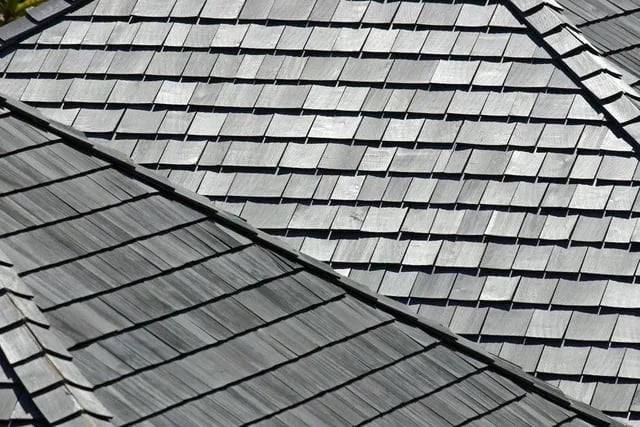 Close-up of a roof showing gray asphalt shingles arranged in overlapping rows with a ridge line visible