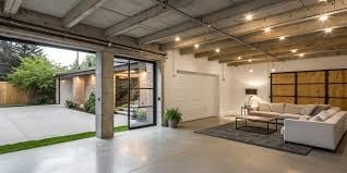 Modern open-plan living space with glass doors opening to outdoor patio, concrete floors, and minimalist furniture