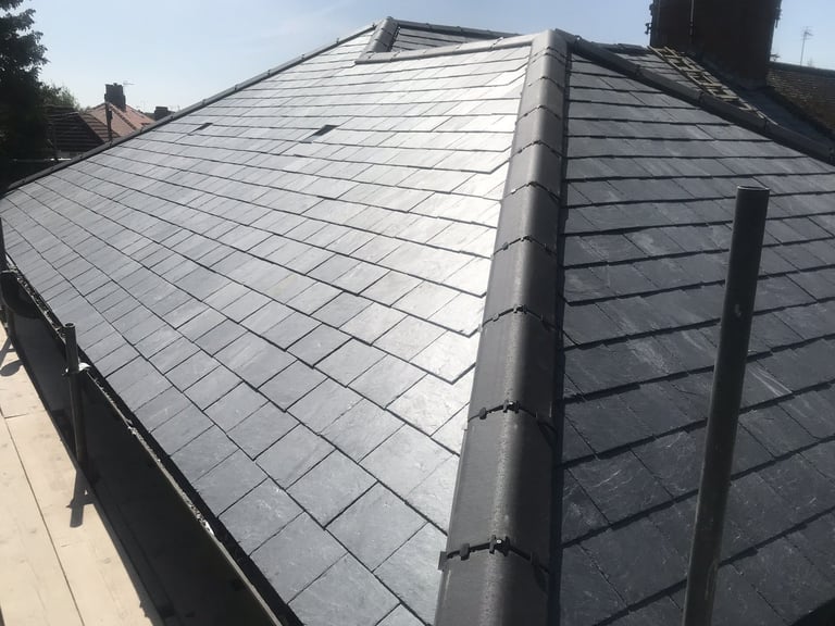 Newly installed gray slate roof tiles on a residential house with a central chimney and metal flashing