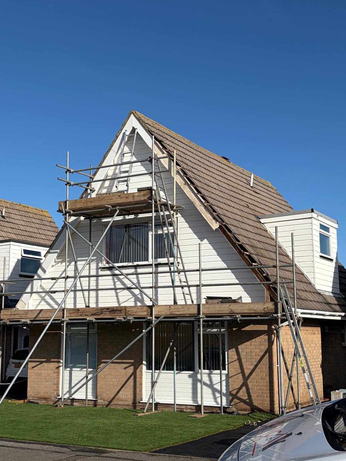 Two-story brick and white house with metal scaffolding during renovation, featuring pitched roof and clear blue sky