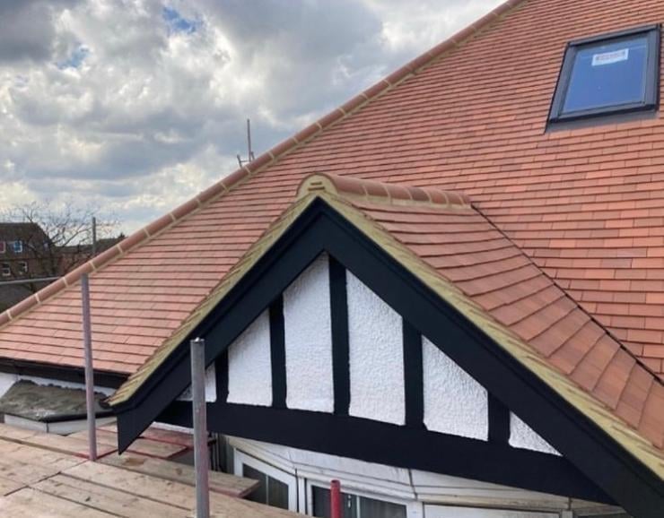 Gabled roof with terracotta tiles and black-and-white timber framing detail against cloudy sky