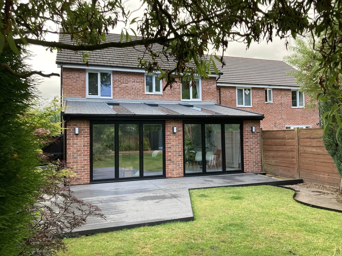 Modern brick house with black-framed glass doors, slate patio, and manicured green lawn surrounded by hedges