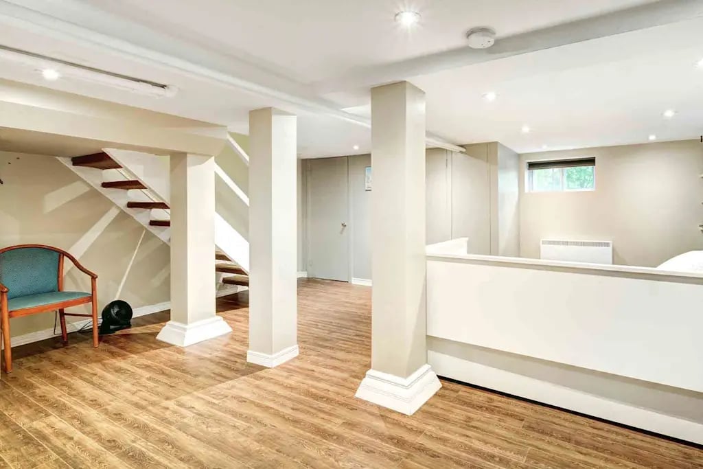 Modern basement with white support columns, wooden flooring, reception desk, staircase, and fitness equipment