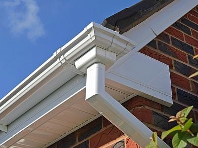 White gutters and downspout on brick house exterior against blue sky