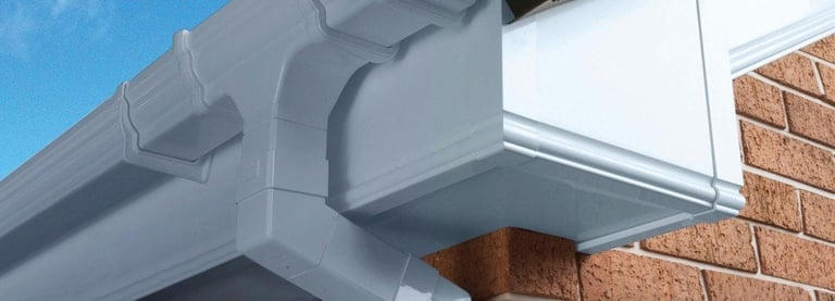 White PVC gutter system installed on brick building exterior with downspout connection