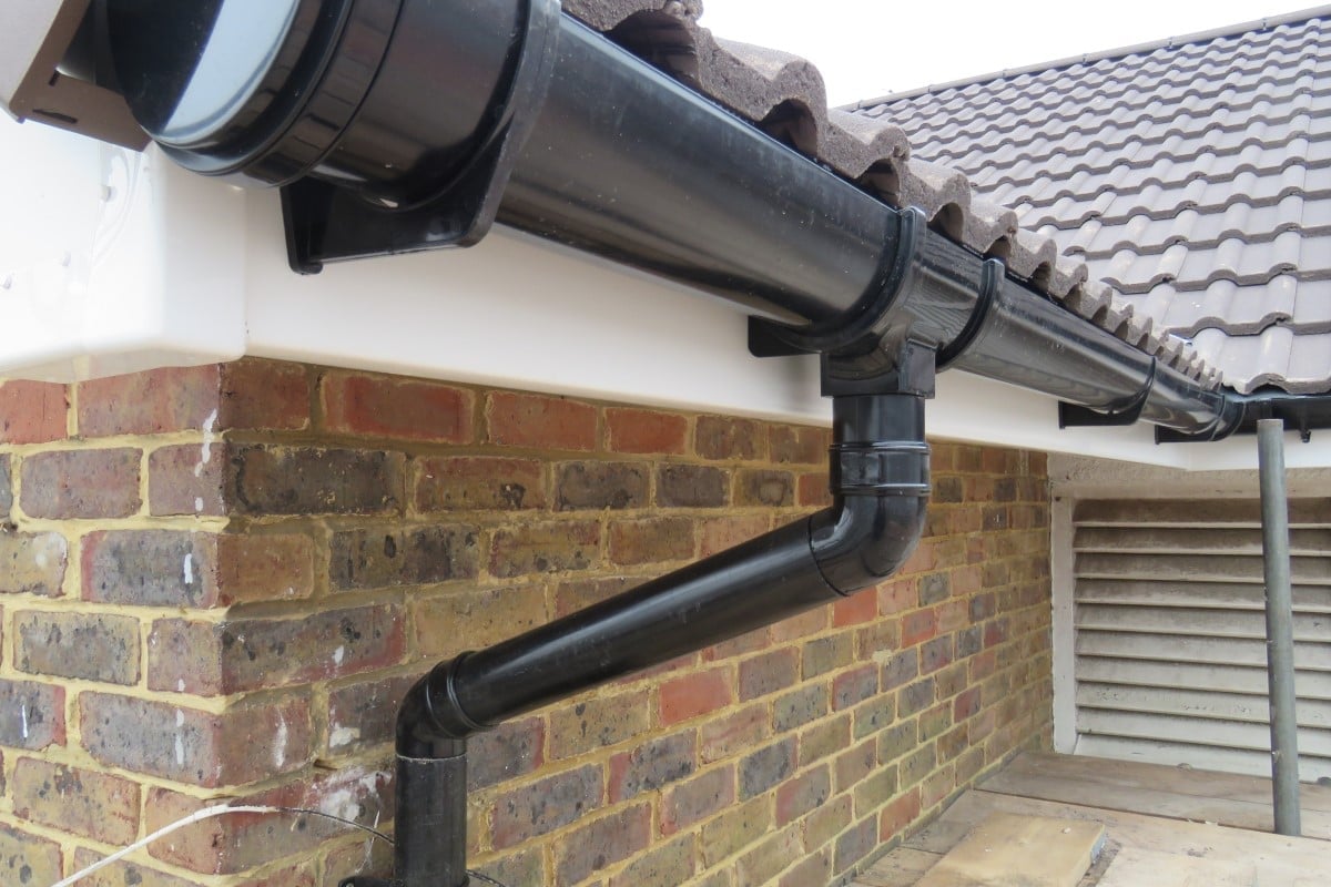 Black downspout and gutter system installed along brick house exterior with tile roof