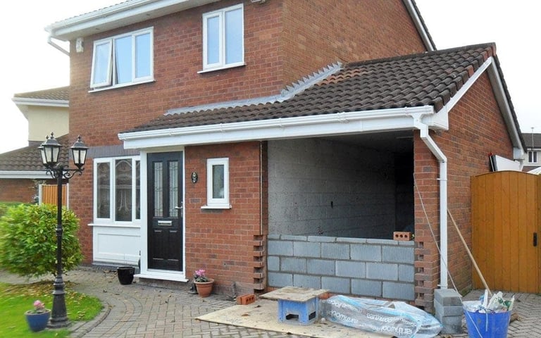 Brick residential house under construction with open garage, white trim, and building materials visible in the driveway